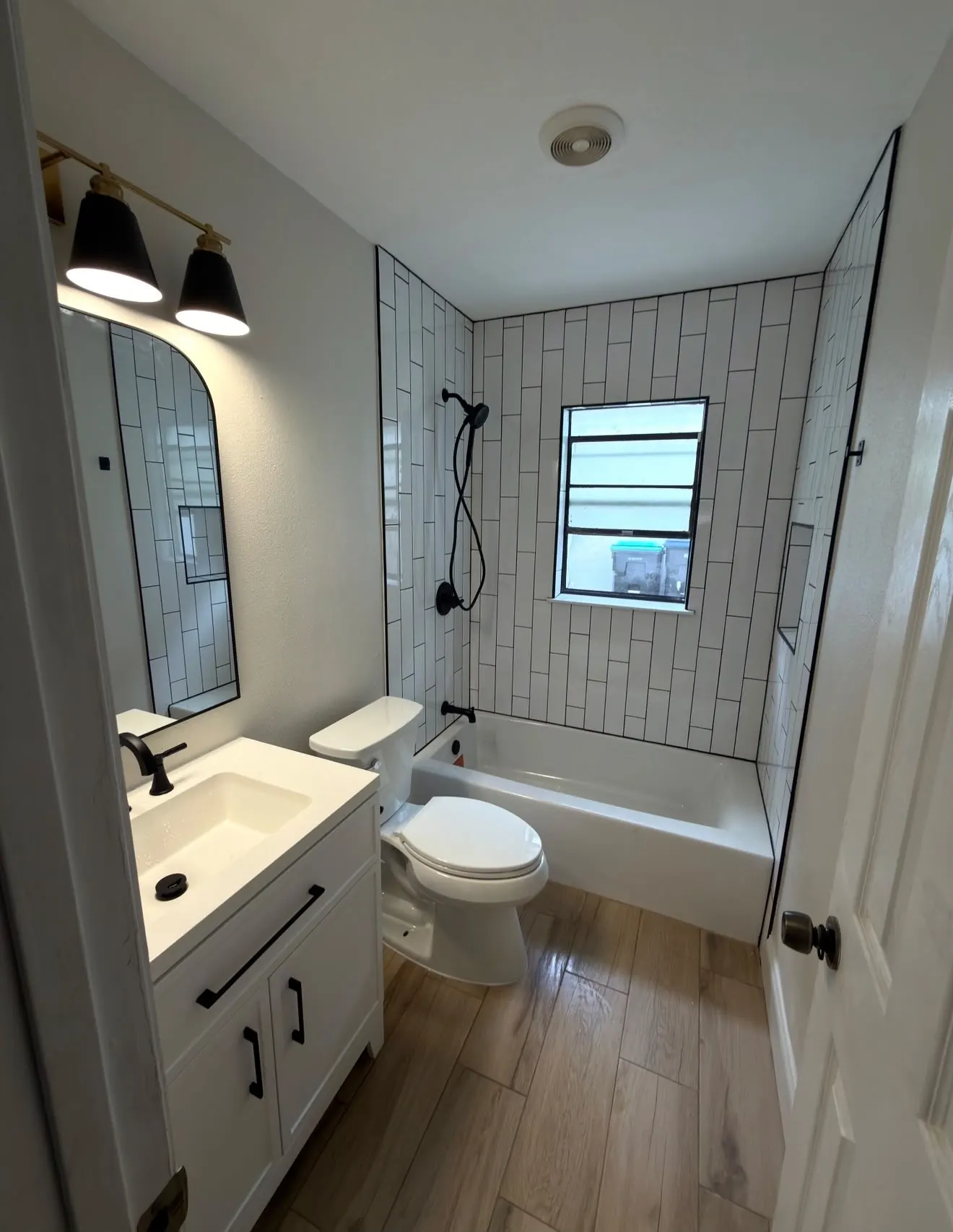 Small bathroom finished in vertical white subway tile with black grout and fixtures